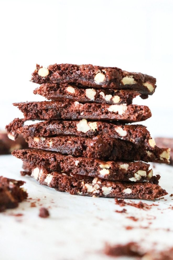 tento obrázek je boční pohled na stoh brownie křehký s ořechy v něm. Stoh sedí na bílém pultu s dalšími křehkými kousky brownie rozmazanými v pozadí.