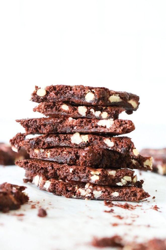 This image is a side view of a stack of brownie brittle with nuts in it. The stack sits on a white counter with other brownie brittle pieces blurred in the background.