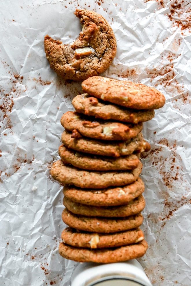 This is an overhead image of a line of gingersnap cookies leaning against a glass of milk. The cookies lay on top of a piece of parchment paper.