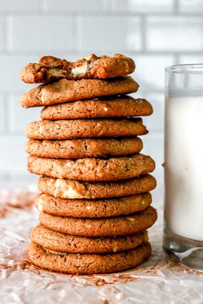 This is a side view of a stack of gingersnap cookies on a counter with a glass of milk. The top cookie has a bite taken out of it.