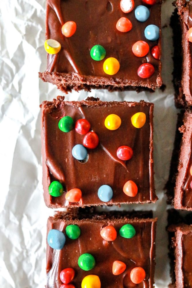 This is an overhead image of cosmic brownies with chocolate frosting and colorful candies on top. The brownies sit on a white piece of parchment paper.