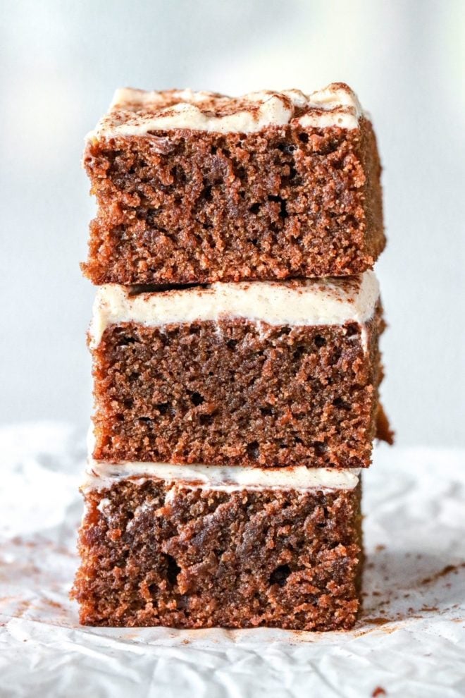 stack of three slices of gingerbread cake with a vanilla icing. the stack sits on a white piece of parchment paper and a white background.