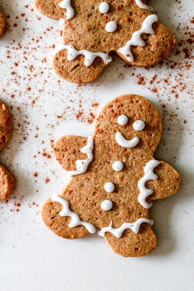 This is an overhead image of gingerbread men cookies with decorative icing. The cookies lay on a white counter and a sprinkle of cinnamon on top.