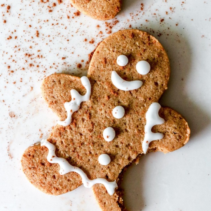 This is an overhead image of a gingerbread man with decorative icing. The cookie has a bite taken out and is laying on a white counter.
