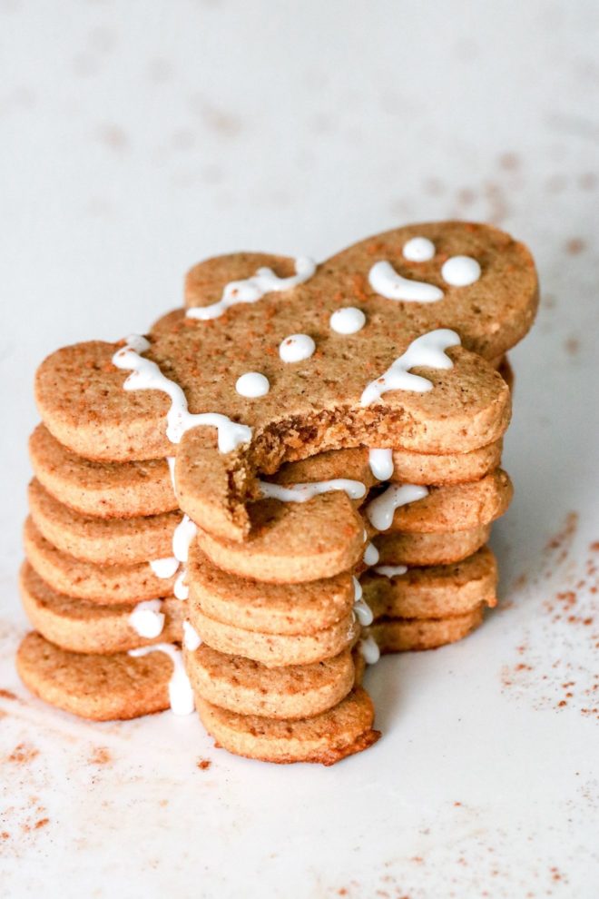 This is a stack of gingerbread men on a white counter. The top gingerbread man has a bite taken out of his leg.