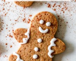 This is an overhead image of a gingerbread man with decorative icing and a sprinkle of cinnamon. The gingerbread man lays on a white counter. The image has text overlay "gluten free gingerbread men cookies."