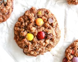 This is an overhead image of monster cookies laying on a white piece of parchment paper. The cookies have oats and M&Ms visible and are sprinkled with some salt.