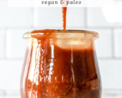 side view of a small glass jar filled with caramel. the jar sits on a white counter with a white background. a spoon drips caramel into the jar. text overlay reads "homemade caramel vegan & paleo"