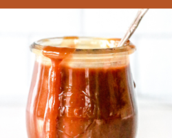 side view of a small glass jar with caramel inside and dripping off the edge. a spoon sticks out of the jar and the jar sits on a white counter with a white background. text overlay reads "vegan & paleo homemade caramel sauce"