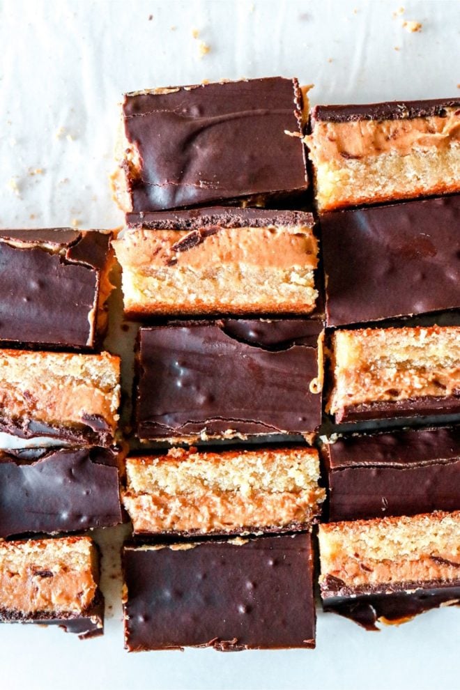 overhead image of peanut butter cookie bars with three layers, a shortbread layer, a peanut butter layer and a chocolate layer. the bars alternate, half are standing on their side so you can see their layers, half have the chocolate side up.