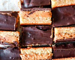 overhead image of peanut butter millionaire bars with three layers, a shortbread layer, a peanut butter layer and a chocolate layer. the bars alternate, half are standing on their side so you can see their layers, half have the chocolate side up. text overlay reads "gluten free peanut butter millionaire bars"