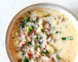 This is an overhead image of a soup bowl on a white counter. The soup has a creamy broth with pieces of meat, kale, and potatoes in it. Text overlay reads "instant pot zuppa toscana"