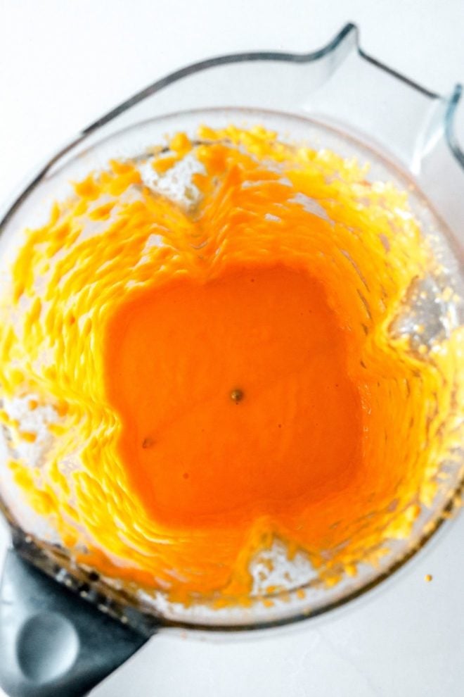 This is an overhead image looking into a blender. Inside the blender is an orange dressing. The blender sits on a white counter.