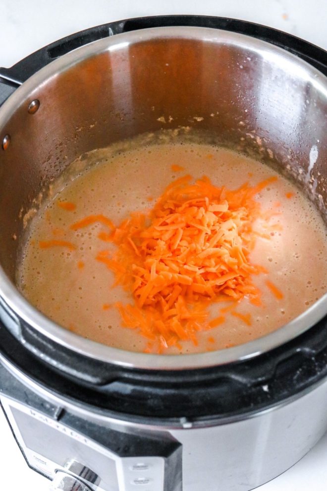 This is an image looking into an instant pot with creamy cauliflower soup. Shredded cheddar cheese is on top of the soup.