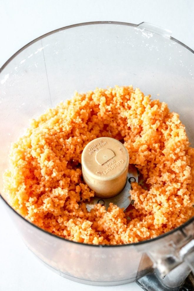 This is an overhead image looking into a food processor with the raw crumbly cracker mixture. The food processor sits on a white counter.