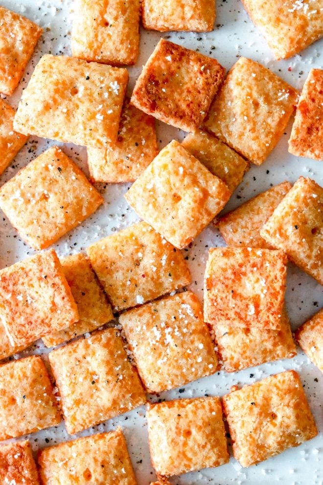 This is an overhead image os square orange crackers on a white piece of parchment paper. The crackers are sprinkled with salt and pepper.