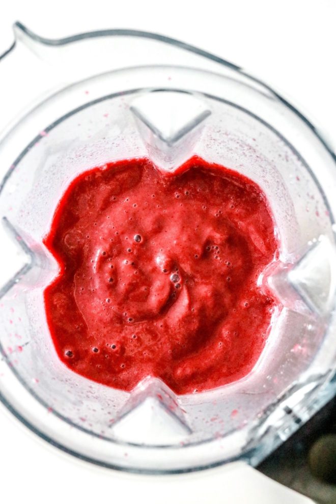 This is an overhead image looking into a blender with cherry smoothie inside. The blender sits on a white counter.