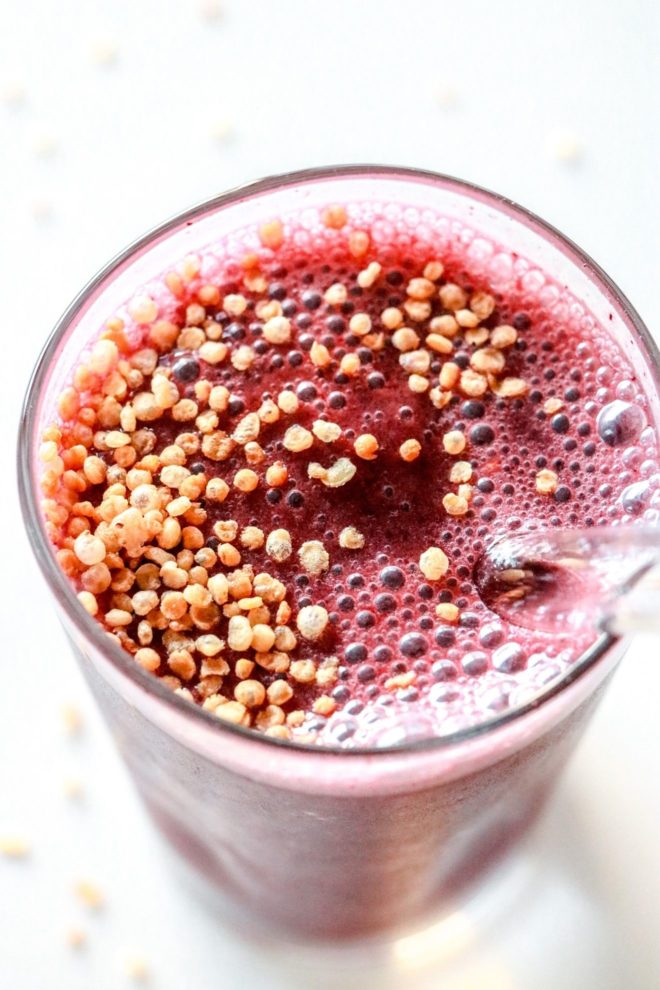 This is an overhead image looking into a glass with a cherry smoothie in it and puffed quinoa. The glass sits on a white counter.