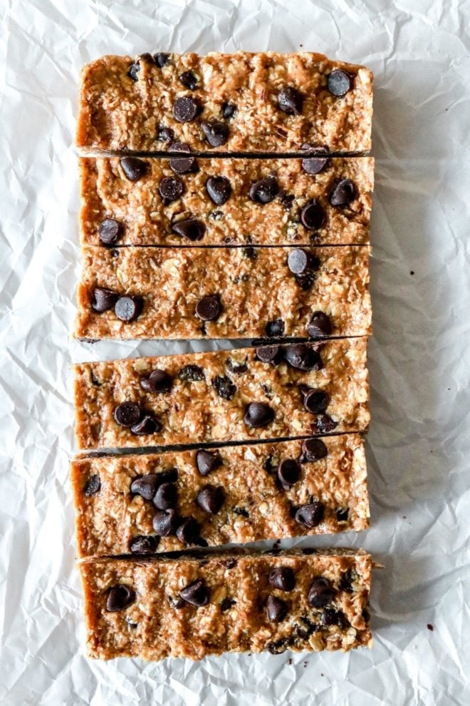 This is an overhead image of six chocolate chip granola bars on a white piece of parchment paper.