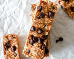 This is an overhead image of chocolate chip granola bars on a white piece of parchment paper. Two bars are stacked on top of each other and other bars are in the corners of the image.
