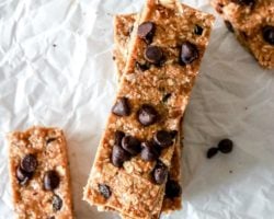 This is an overhead image of chocolate chip granola bars on a white piece of parchment paper. Two bars are stacked on top of each other and other bars are in the corners of the image. Text overlay reads "vegan & gluten free granola bars."