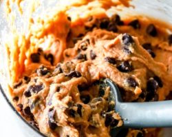 This is an overhead image looking down into a food processor filled with chocolate chip cookie dough. A rubber spatula is sticking out of the food processor. The food processor sits on a white counter.