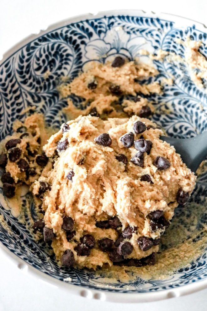 This is an image of a bowl with a blue and white pattern. Inside the bowl is raw chocolate chip cookie dough.