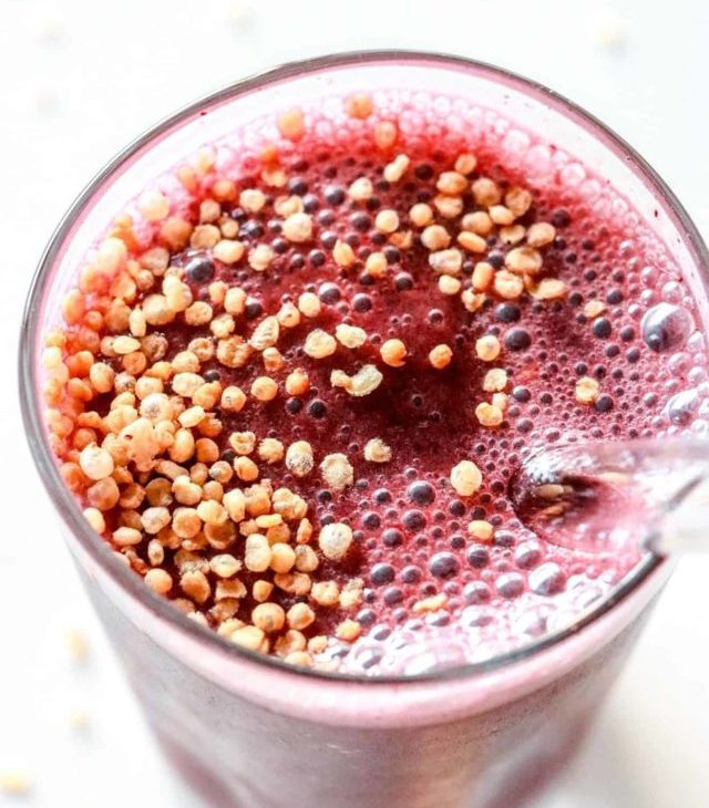 This is an overhead image looking into a glass with a cherry smoothie in it and puffed quinoa. The glass sits on a white counter.