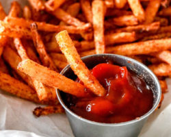 This is a close up image of jicama fries being dipped in ketchup. More fries are on the plate, blurred in the background.