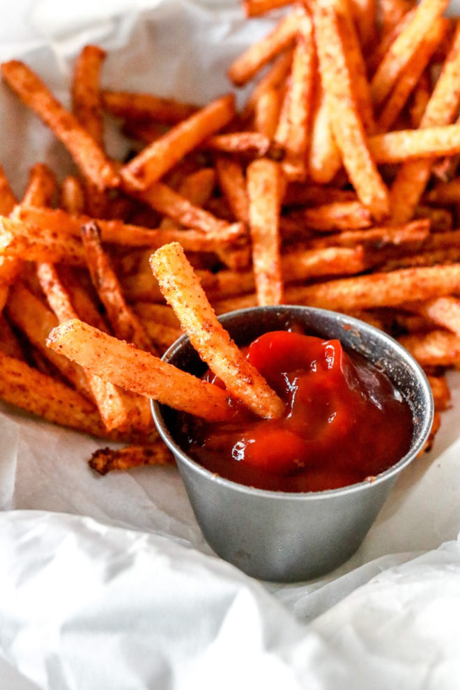 This is a close up image of jicama fries being dipped in ketchup. More fries are on the plate, blurred in the background.
