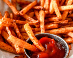 This is a close up image of jicama fries being dipped in ketchup. More fries are on the plate, blurred in the background. Text overlay reads "crispy & delicious jicama fries."
