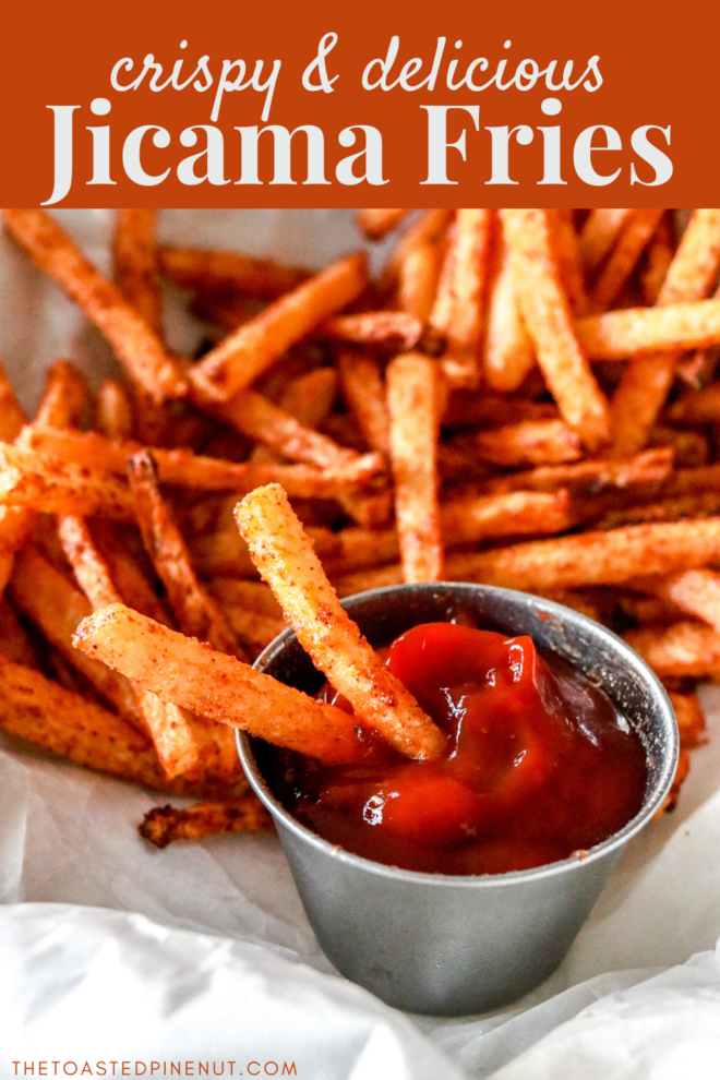 This is a close up image of jicama fries being dipped in ketchup. More fries are on the plate, blurred in the background. Text overlay reads "crispy & delicious jicama fries."