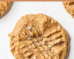 This is a close up image of a peanut butter cookie with fork imprints and salt on top. The cookie sits on a white counter. text overlay reads "peanut butter cookies refined sugar free & gluten free."