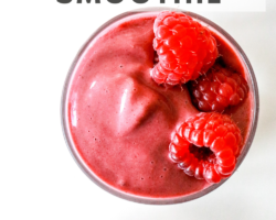 This is an overhead image of a raspberry smoothie in a glass on a white counter. Fresh raspberries are at the top and bottom of the image. Text overlay reads "the best raspberry smoothie."