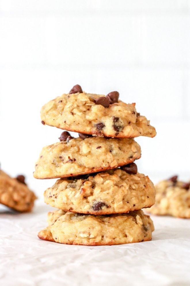 This is a side view of a stack of four oatmeal chocolate chip cookies sitting on a white counter. More cookies are blurred in the background.