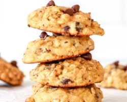 This is a side view of a stack of four oatmeal chocolate chip cookies sitting on a white counter. More cookies are blurred in the background.