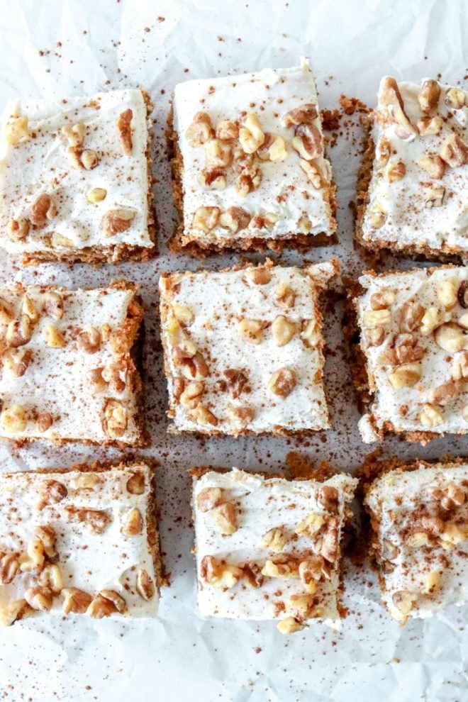 This is an overhead image of nine carrot cake bars with cream cheese frosting. The bars are topped with chopped walnuts and a sprinkle of cinnamon.