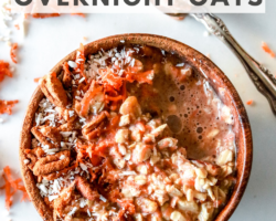 This is an overhead image of a small wood bowl with carrots, oats, pecans, and shredded coconut in it. A spoon full of oatmeal is off to the right top of the image. More shredded carrot and nuts are on the counter around the bowl. Text overlay reads "vegan & gluten free carrot cake overnight oats."