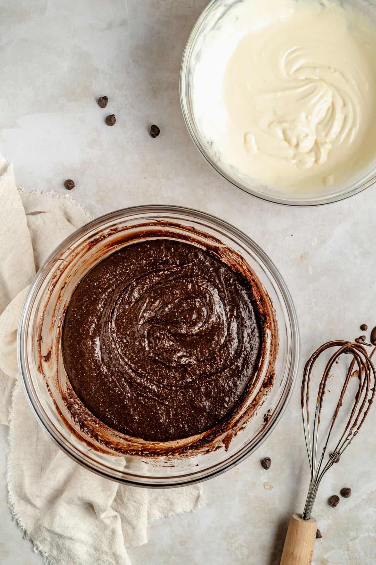 This is an overhead image of brownies with a cheesecake swirl. The brownies are cut into squares and sit on a white piece of parchment paper on a white counter. A knife is in the bottom corner of the image.