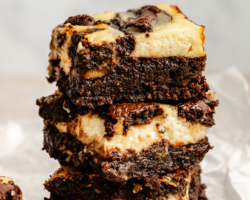 This is a stack of three brownies on a white counter and white background. The brownies have a cheesecake layer. Text overlay reads "Fudgey Cheesecake Brownies flourless & gluten free"
