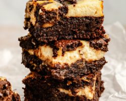This is a stack of three brownies on a white counter and white background. The brownies have a cheesecake layer.