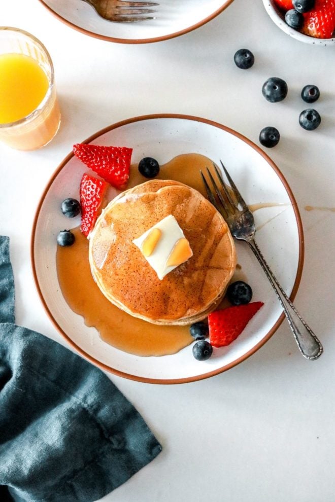 This is an overhead image of oat flour pancakes on a plate with strawberries and blueberries. The pancakes have a pad of butter and syrup on them.