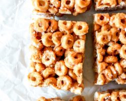 This is an overhead image of peanut butter cheerio bars. The bars are cut and sprinkled in salt. The bars sit on a white piece of parchment paper.