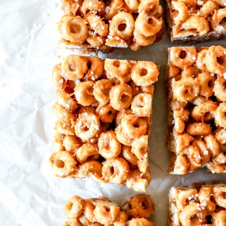 This is an overhead image of peanut butter cheerio bars. The bars are cut and sprinkled in salt. The bars sit on a white piece of parchment paper.