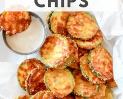 This is an overhead image of a plate of zucchini chips on top of parchment paper. There is a small bowl of ranch dressing to the top.