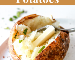 This is an overhead view of a baked potato cut in half. Inside the potato is some melted butter, freshly ground pepper and fresh herbs. The potato sits on a white plate and a fork is digging into the potato. Text overlay reads "air fryer baked potatoes."