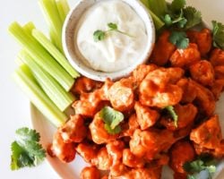 This is an overhead image of a plate with buffalo cauliflower florets. The plate also has a small bowl of blue cheese dip and celery sticks.