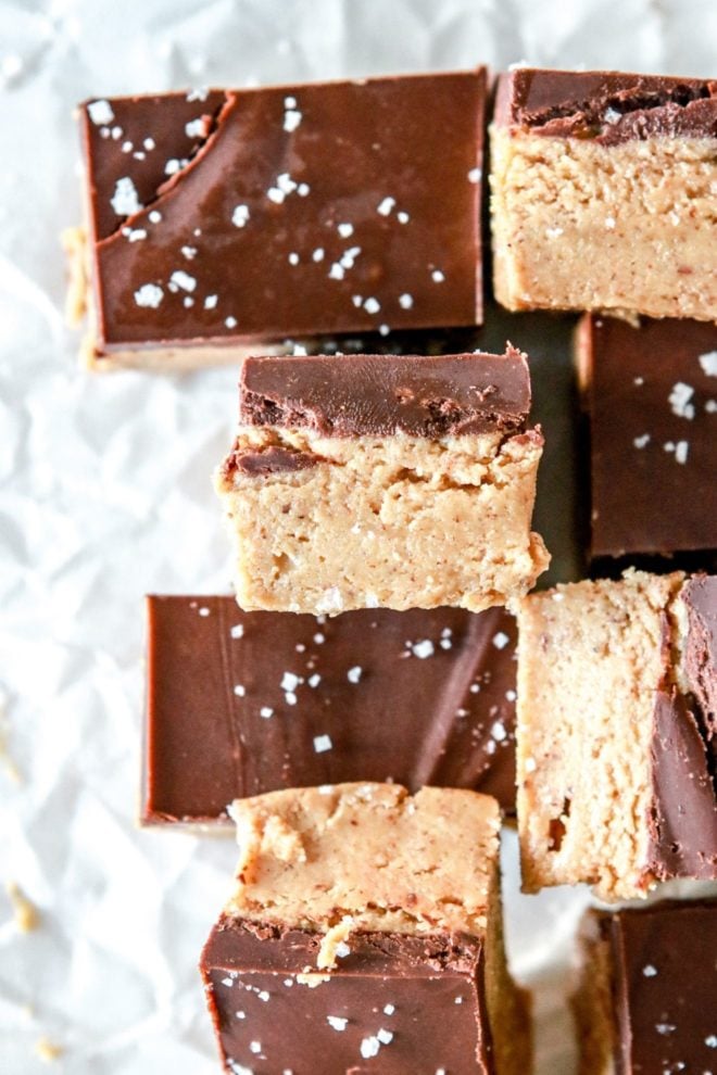 This is an overhead image of chocolate almond butter bars. Some bars are tilted on the side to show the middle of the bars. The bars are on a white piece of parchment paper and sprinkled with salt.