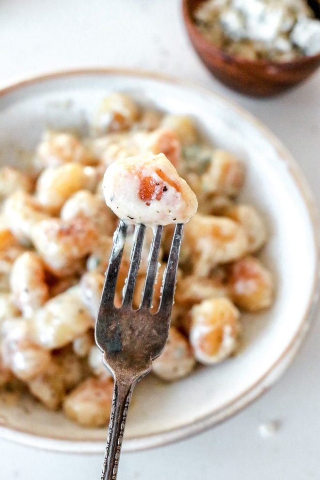 This is an overhead image of a bowl with gnocchi and gorgonzola sauce. A fork is piercing a gnocchi and holding in focus while the bowl is out of focus in the background.