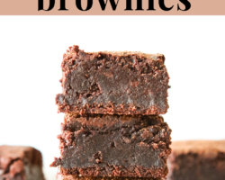 This is a stack of three fudgey brownies. The brownies sit on a white piece of parchment paper and a white background. More brownies are blurred in the background. Text overlay reads "intensely fudgey oat flour brownies."